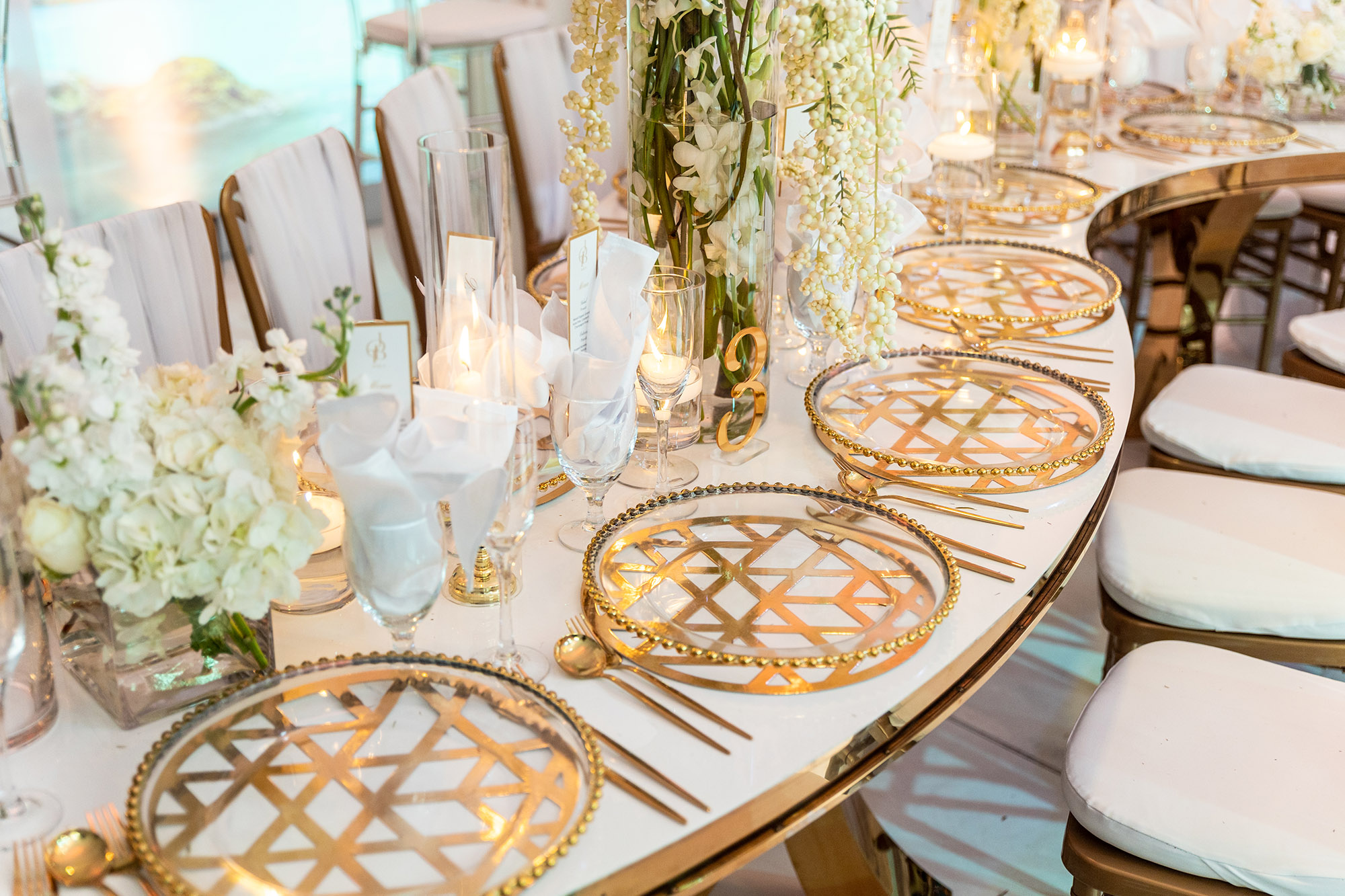 White flower arrangements with gold accents on plate settings, silverware, tables and chairs under tent eccessories by ellen www.eccessoriesbyellen.com