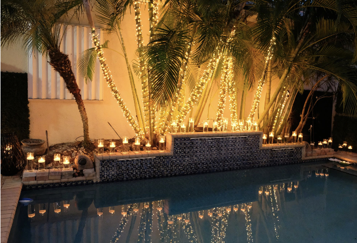 Floating candle lighting around a pool at night with tree lighting- eccessories by ellen www.eccessoriesbyellen.com