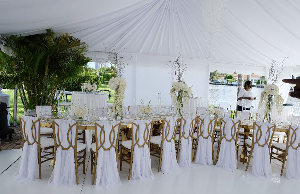 White flower arrangements with gold accents on plate settings, silverware, tables and chairs under tent eccessories by ellen www.eccessoriesbyellen.com