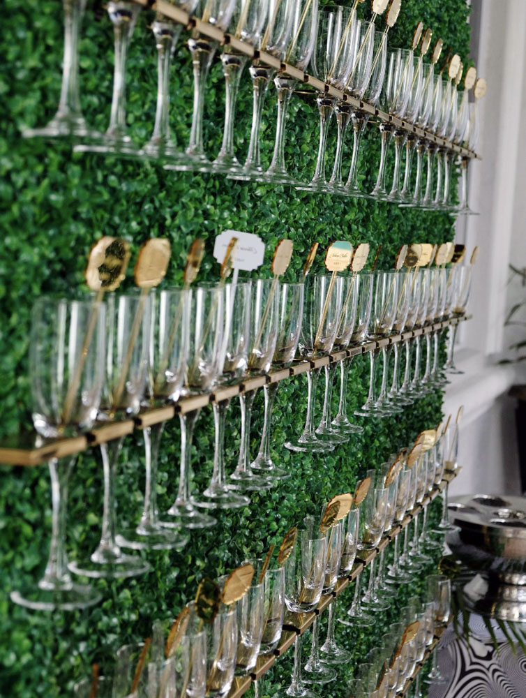 A wedding reception table allocation placing keys in elegant wine glass wall display with green foliage eccessories by ellen www.eccessoriesbyellen.com