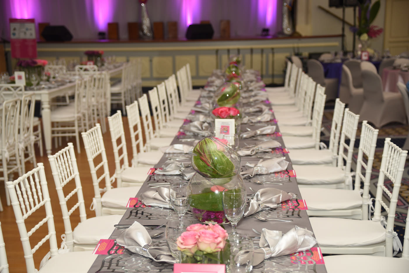 Long silver table with purple and pink flowers in vases and silver plate settings eccessories by ellen