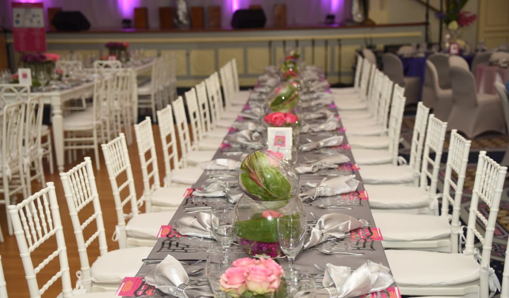 Long silver table with purple and pink flowers in vases and silver plate settings eccessories by ellen